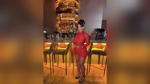 Elegant woman in a red lace cocktail dress posing at a luxury dimly lit bar with high stools.