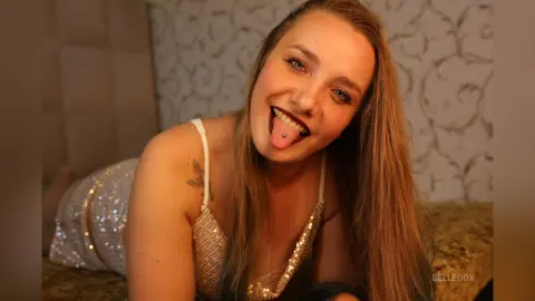 Smiling young woman in a sparkling sequin dress relaxing in a cozy room with patterned wallpaper.