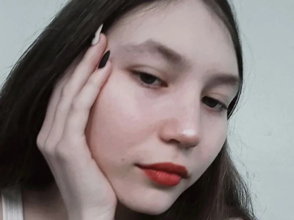 Close-up portrait of a young woman with long dark hair and red lipstick looking thoughtfully at the camera.