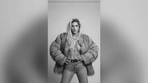 JessycaPage poses in a large fur coat and jeans, looking at the camera with long blonde hair.