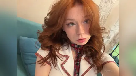 Redheaded woman in a white and red schoolgirl outfit sitting on a blue sofa with a soft, dreamy mood.