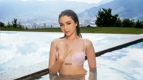 Young woman in a pink bikini relaxing in a luxury infinity pool overlooking a scenic mountain city view.