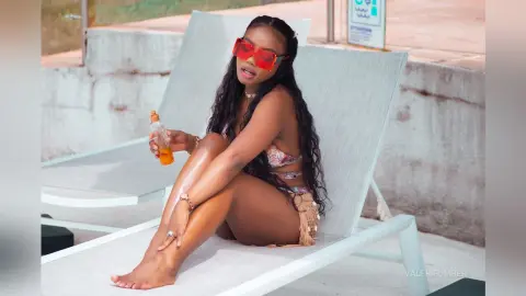 Young woman in a patterned bikini relaxing on a white lounge chair at a sunny outdoor pool area.