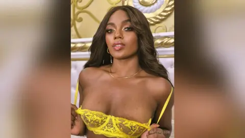 Beautiful woman in a yellow lace bralette posing with a confident expression in a bright indoor setting.