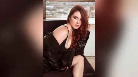 Glamorous woman in a black leather jacket and tank top posing with a confident mood in a modern indoor setting.