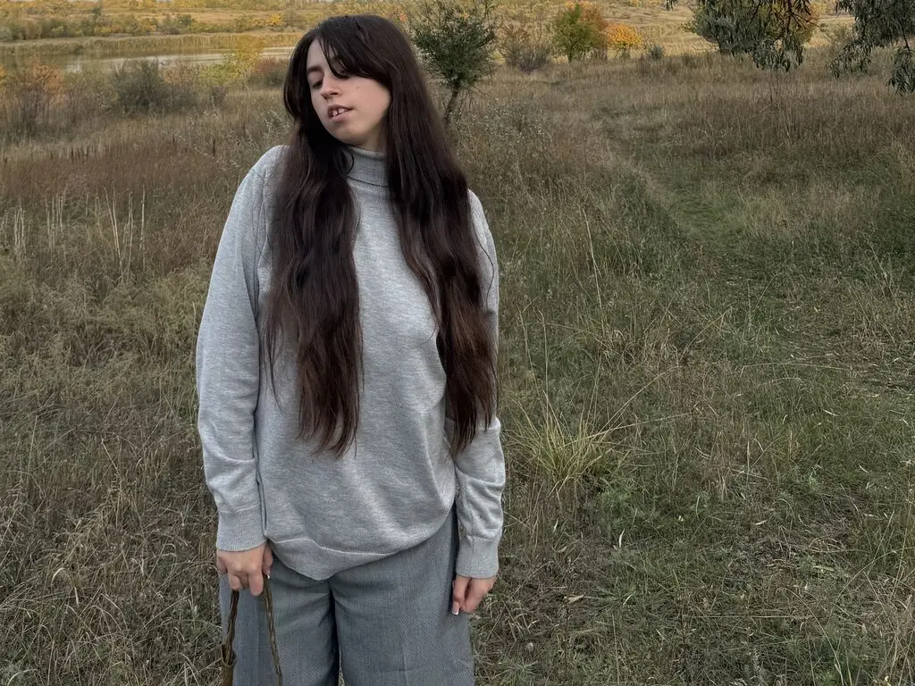 Young woman with long dark hair wearing a grey turtleneck sweater in a moody autumn meadow field.
