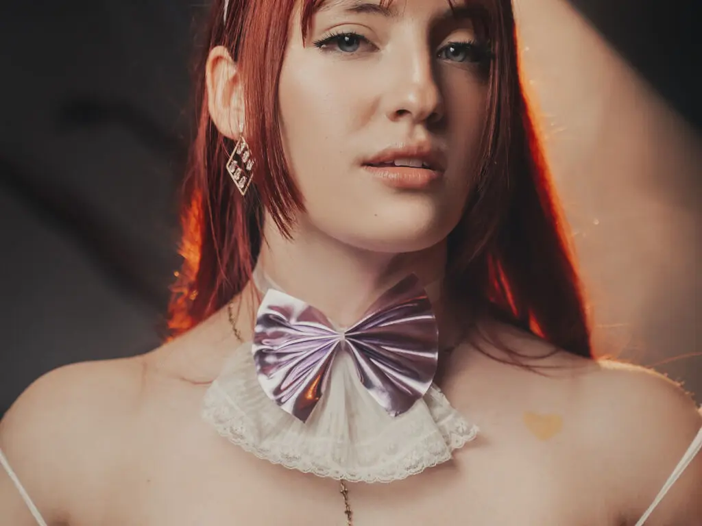 Redheaded woman in a white lace outfit and purple satin bow choker posing with a soft, dreamy mood.