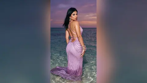 Elegant woman in a lavender sequin backless gown standing in ocean water at sunset.