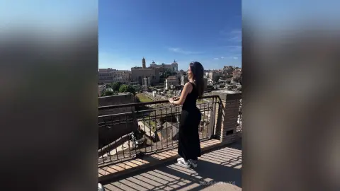 Stylish woman in a black dress overlooking the ancient Roman Forum ruins under a clear blue sky.