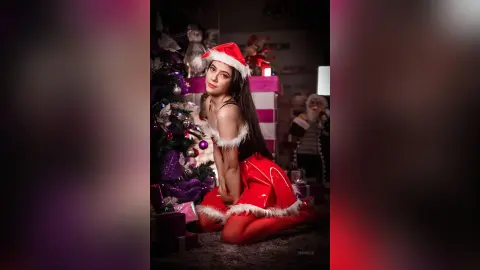 JessieLiu poses in a red and white Santa outfit, sitting on the floor next to a decorated Christmas tree.