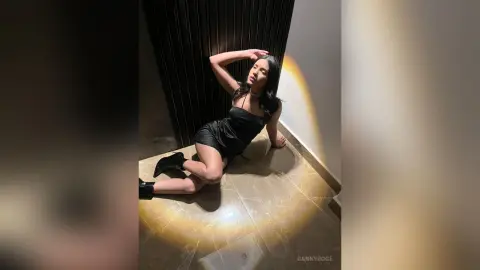 Elegant woman in a black cocktail dress sitting on a marble floor in moody, dramatic lighting.
