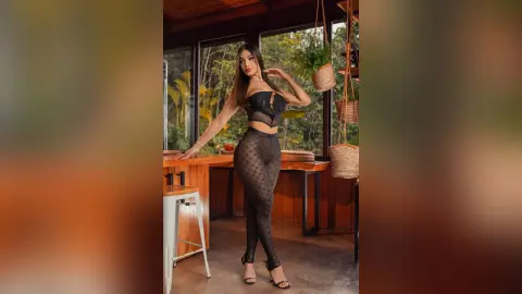 Glamorous woman in a black corset and patterned leggings posing in a tropical sunlit room.