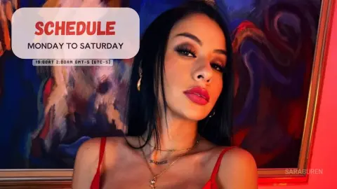 Young woman with long dark hair and gold jewelry posing against an abstract painting background.