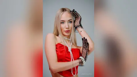 MarryDavies poses with her hands near her face wearing a red satin top, white pearls, and black lace gloves.