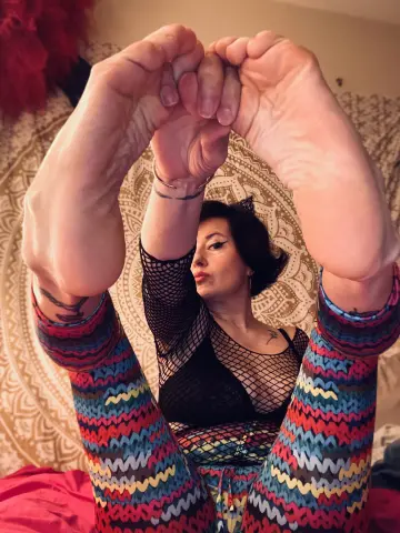 Woman in black lace top and colorful patterned leggings relaxing on a patterned rug with feet raised.