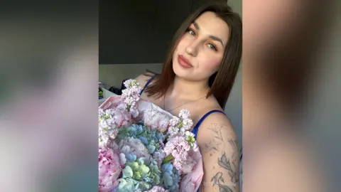 BettyBlossom — BettyBlossom poses with a large bouquet of pink and blue flowers while wearing a blue strap top.