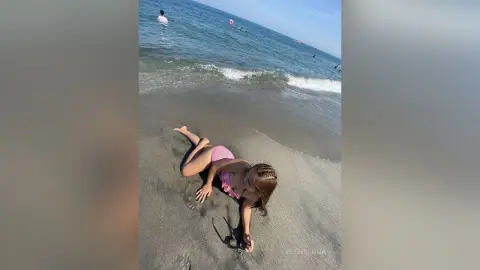 Young girl in a pink bikini relaxing on a sunny sandy beach by the ocean waves.