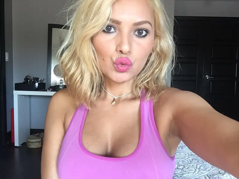 MariPossaxxx smiles with her blonde hair down, wearing a patterned bikini top while posing in front of a bright window.