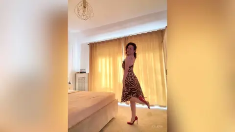 Selena — Elegant woman in a brown animal print dress posing in a bright, modern bedroom.