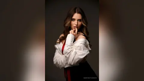 Elegant woman in a white puff-sleeve blouse posing thoughtfully against a dark studio background.
