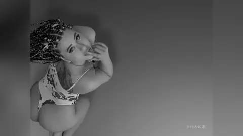 Black and white portrait of a smiling woman in a patterned bodysuit posing in a minimalist studio setting.