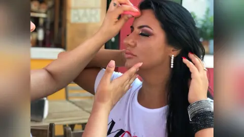 MissyJolie has long black hair and heavy eye makeup while a hand applies pink blush to her cheek.