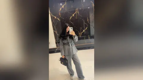 Young woman in a grey linen co-ord set posing in a modern marble hallway for a stylish mirror selfie.