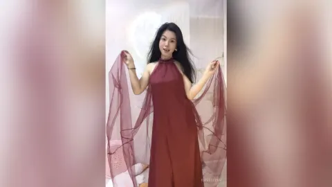 KireliaYan — KireliaYan poses in a long maroon halter dress with sheer flowing fabric held out by her hands.