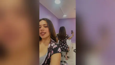 Young woman in a black floral print top smiling in a modern purple room.