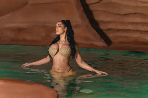 Serene woman in a beige bikini relaxing in a natural desert oasis pool against red rock cliffs.