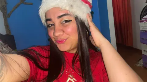 Smiling woman in a red shirt and white Santa hat posing indoors for a festive holiday selfie.