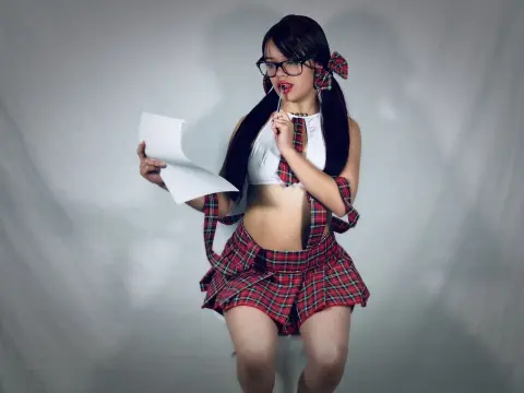Young woman in red plaid schoolgirl cosplay holding paper against a plain studio background.