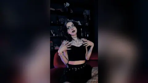 Goth woman in black crop top and lace outfit posing in a moody, dark aesthetic room.