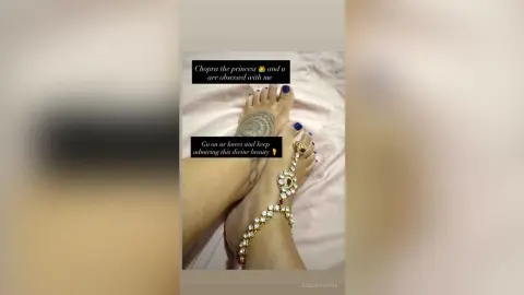 Close-up of bare feet with blue nail polish and a gold anklet resting on a white bedsheet.