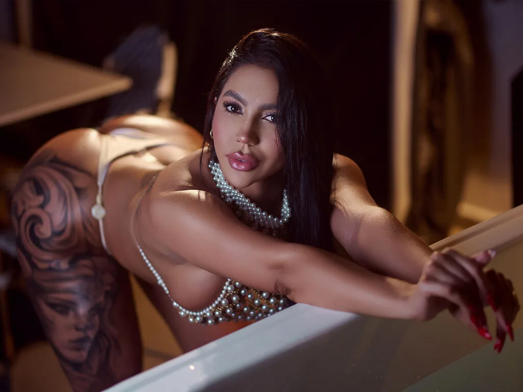 OrianaRossy leans over a white bathtub wearing a pearl bikini and showing off her large hip tattoos.