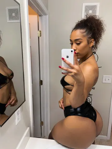 Curvy woman in a black bikini taking a mirror selfie in a modern bathroom.