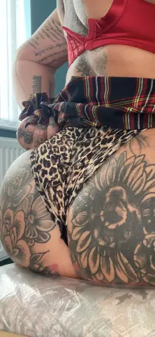 Curvy woman with large floral tattoos wearing leopard print bikini bottoms and a red bra in a bright room.