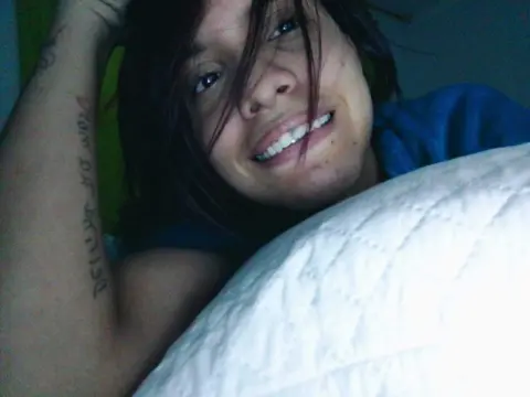 Smiling young woman with dark hair relaxing on a white pillow in a cozy indoor setting.