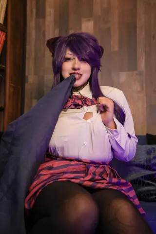 Cosplayer in school uniform with purple hair sitting on a sofa in a cozy indoor setting.