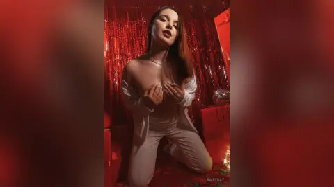 Young woman in white outfit posing against red tinsel backdrop in a glamorous, moody setting.