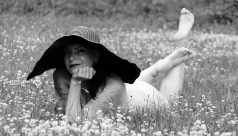 Smiling woman in a wide-brimmed sun hat lying relaxed in a dreamy wildflower meadow.