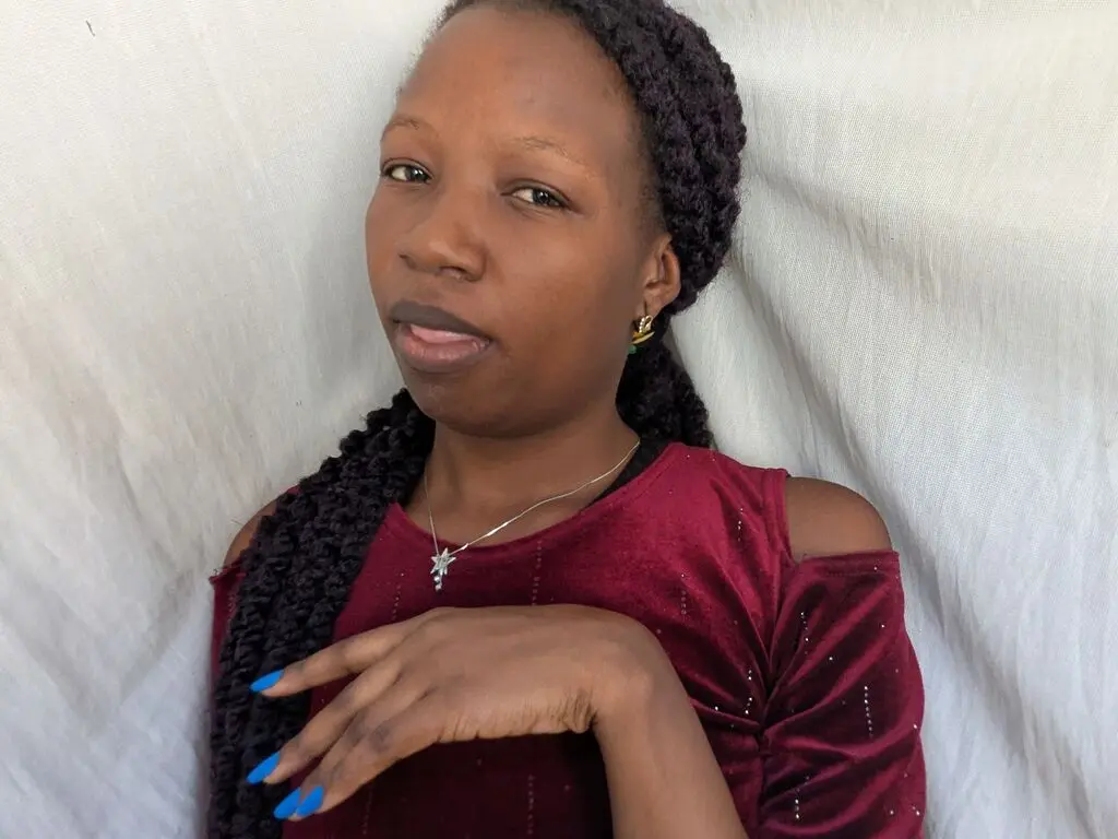ShadiahLov poses with her long black braids and a red velvet top against a white cloth background.