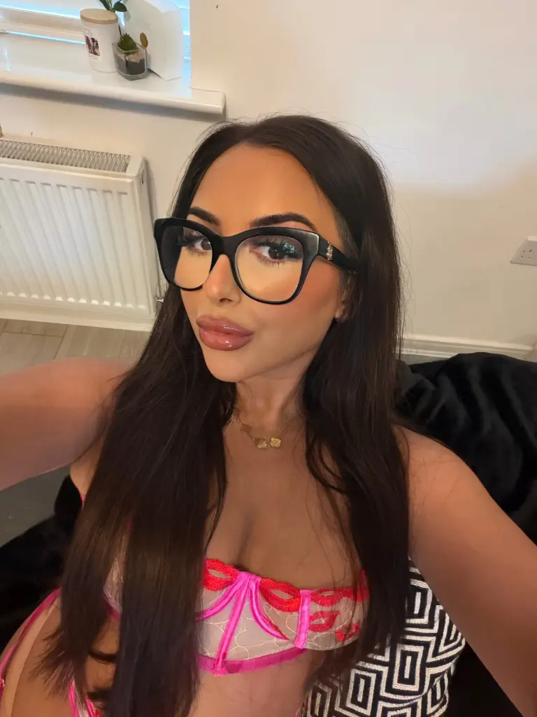 Bonniemaexx poses with long wavy dark hair and black glasses, looking directly at the camera in a close-up shot.