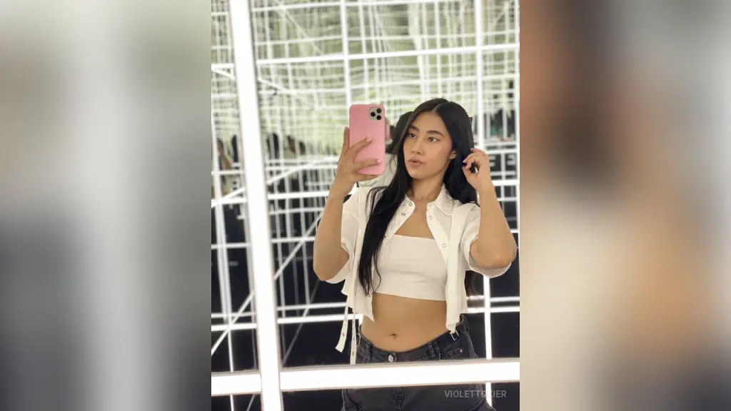 Young woman with long dark hair taking a close-up selfie in a warm indoor setting.