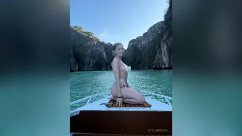 Young woman in a white bikini sitting on a boat in turquoise tropical ocean waters near limestone cliffs.