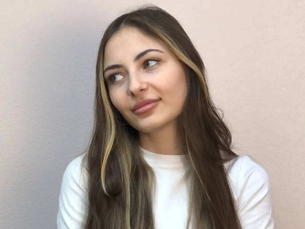 Smiling young woman with long brown hair wearing a white t-shirt against a neutral background.