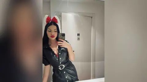 VesperMuse poses in a mirror wearing a black leather button-down dress and red and white ears, holding a phone to take a selfie.