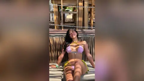 Smiling woman in a lavender bikini relaxing on a wooden beach lounge during a sunny summer vacation.