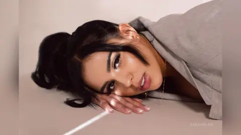 Beautiful woman with dark hair in a grey blazer lying on a neutral background with a soft, elegant mood.
