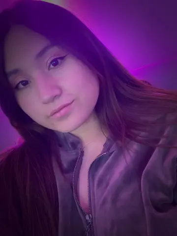 MiaHarveyyy poses with long brown hair wearing a grey zip-up jacket under purple lighting.
